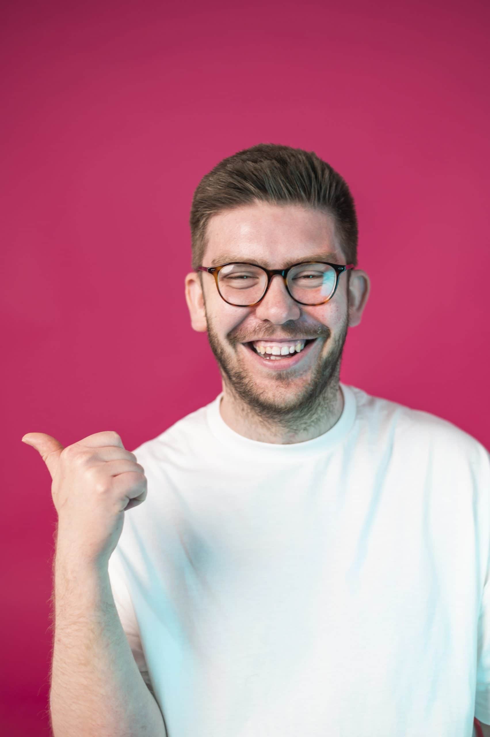Smiling man in glasses gives thumbs up in front of pink background, symbolizing positive feedback at Salience marketing...