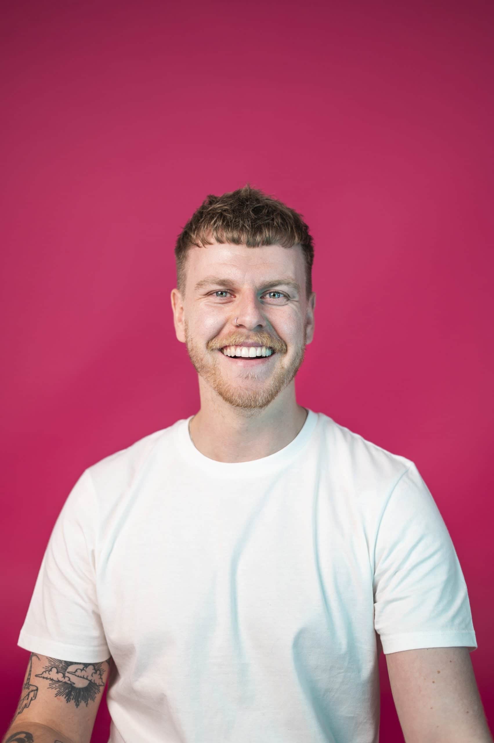 Smiling man in a white t-shirt against a vibrant pink background at Salience marketing agency.
