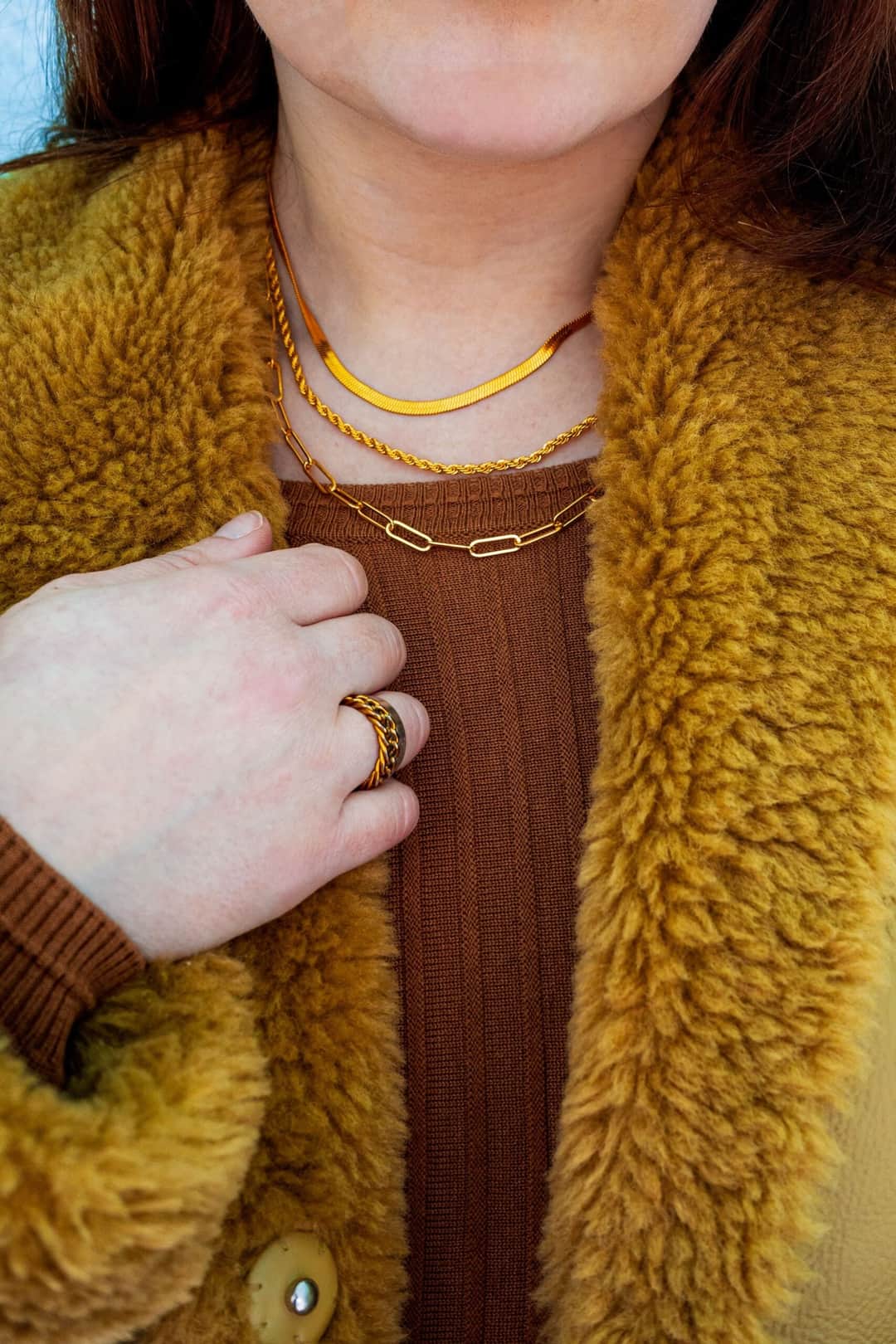Close-up of gold accessories on a warm winter outfit, highlighting necklaces and rings. (Photo: Rachel Brooks via Pexels)