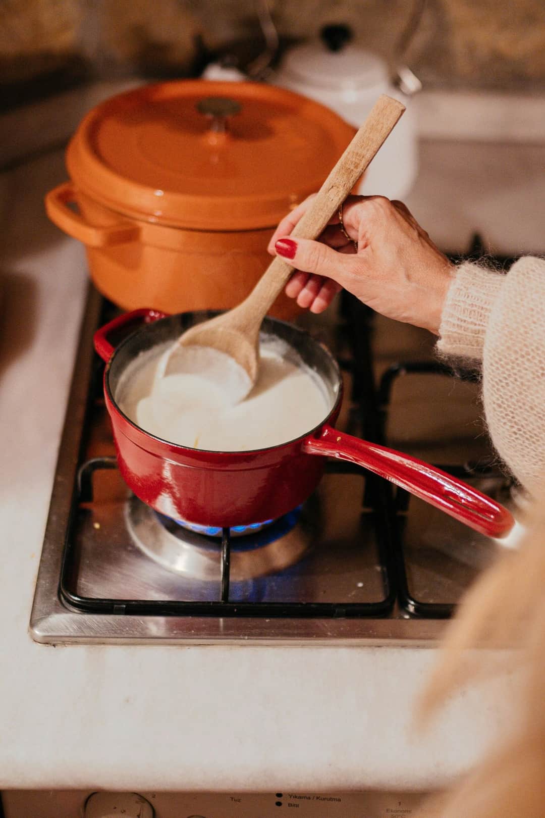 A person stirs milk in a red saucepan on a kitchen stove. Warm, cozy atmosphere. (Photo: furkanfdemir via Pexels)