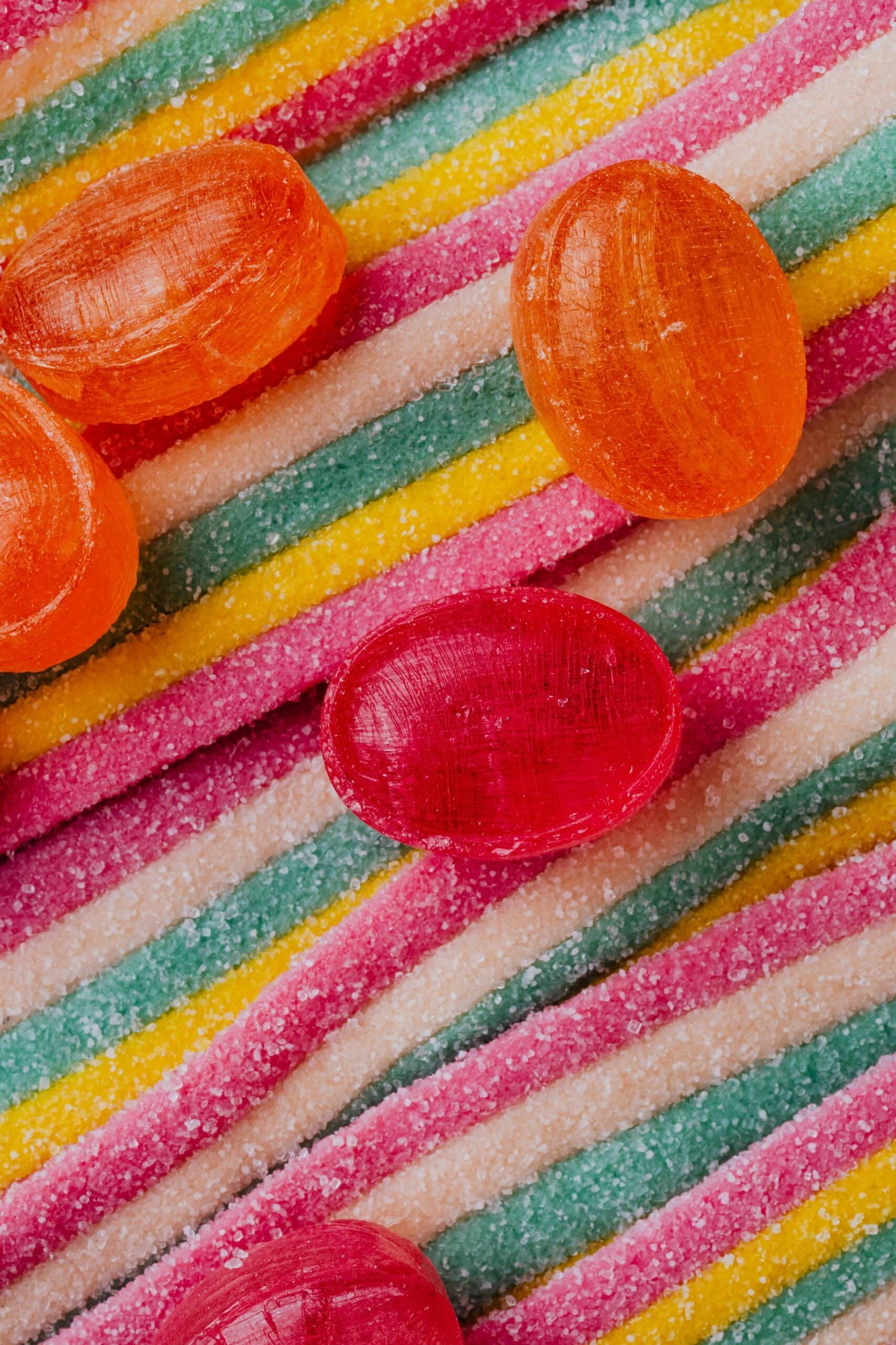 Colorful striped candy background with red and orange hard candies on top.