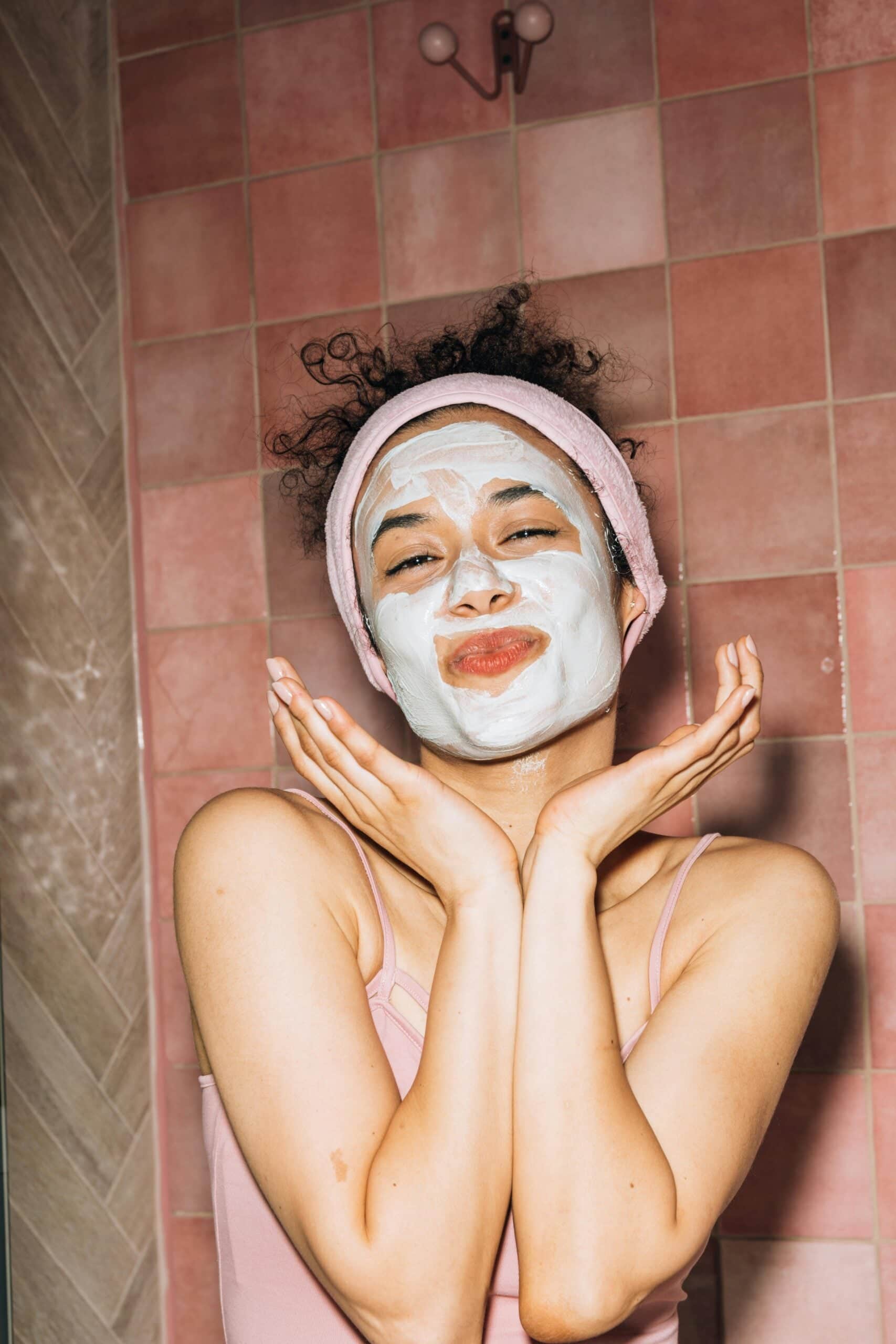 Woman wearing white skincare mask with hands near face in bathroom