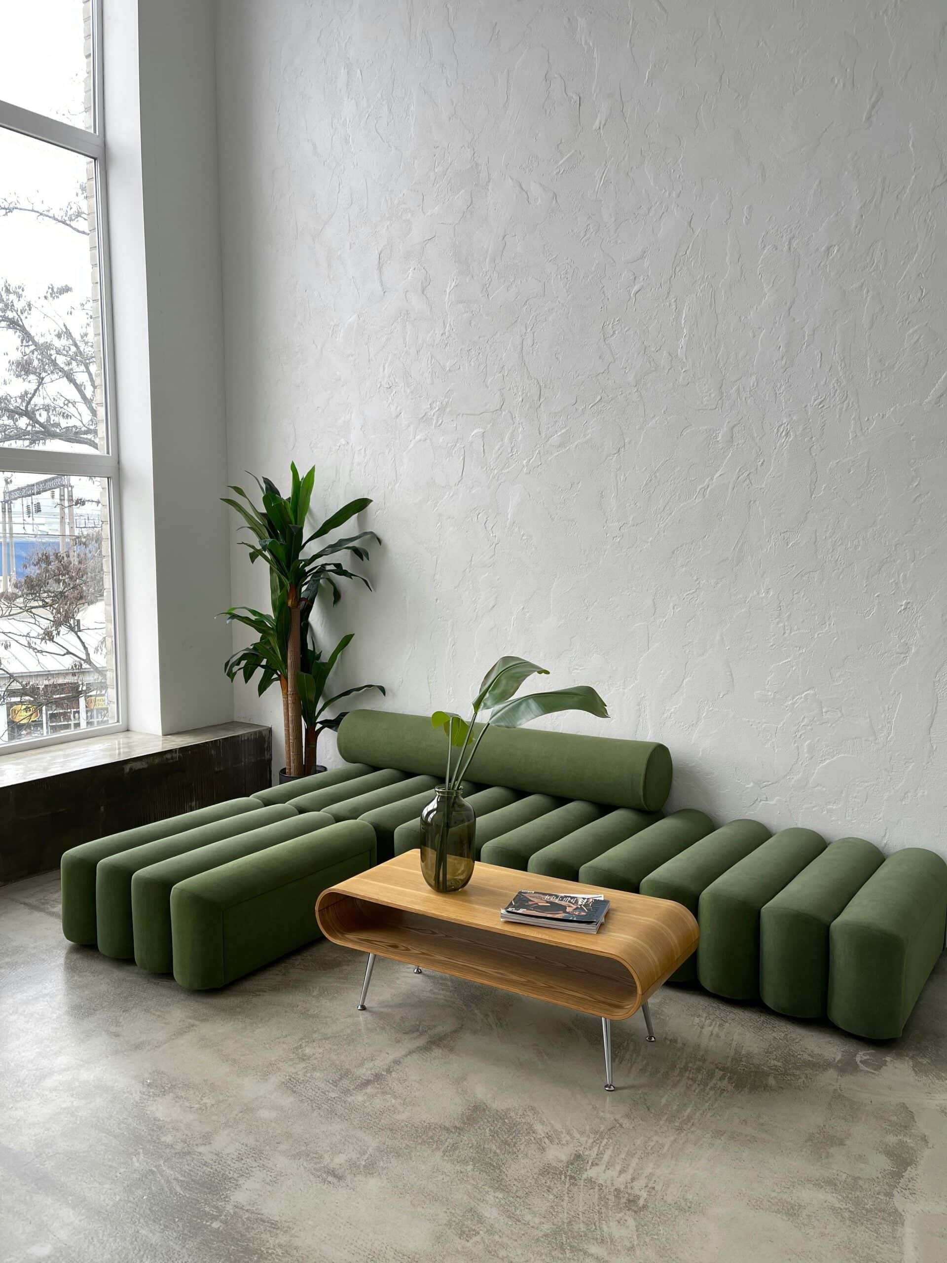 Modern office lounge with emerald green channel-tufted sofa, wooden coffee table, and potted plants