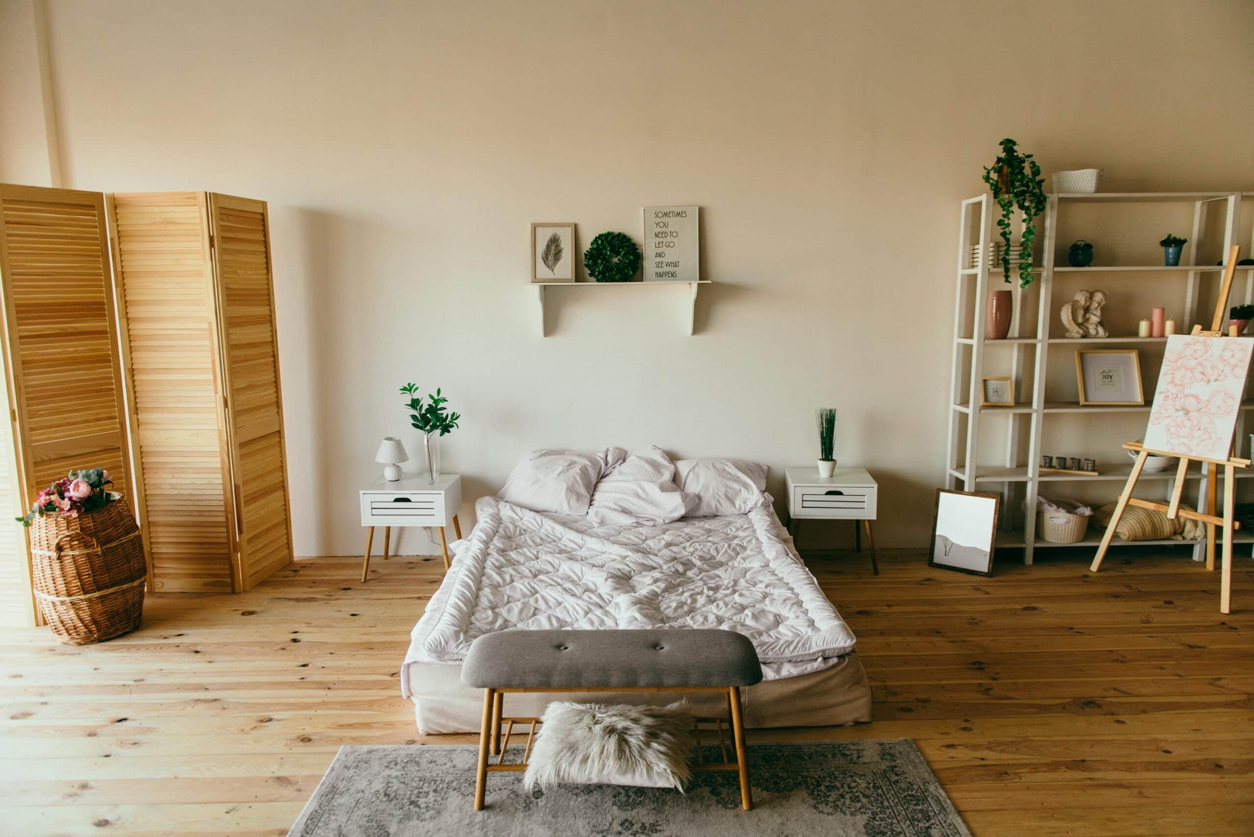 Modern minimalist bedroom interior with wooden floors, white bedding, potted plants, and wall shelving