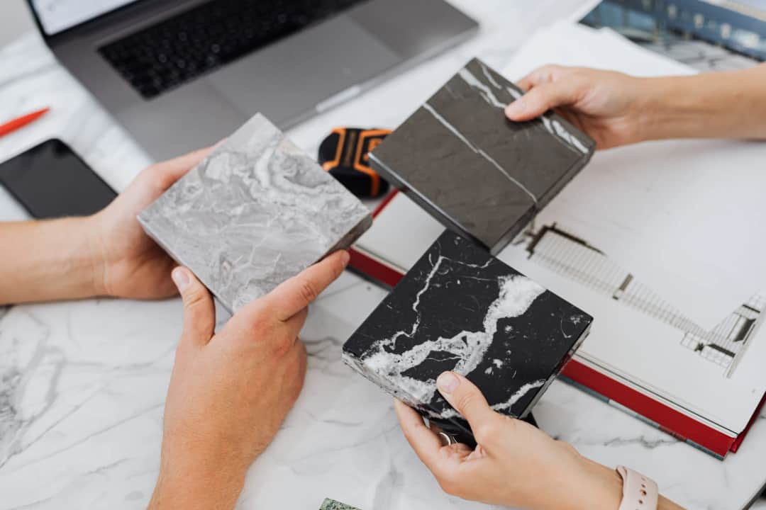 Two architects selecting marble tile samples on a desk in an office setting. (Photo: https://kaboompics.com/ via Pexels)