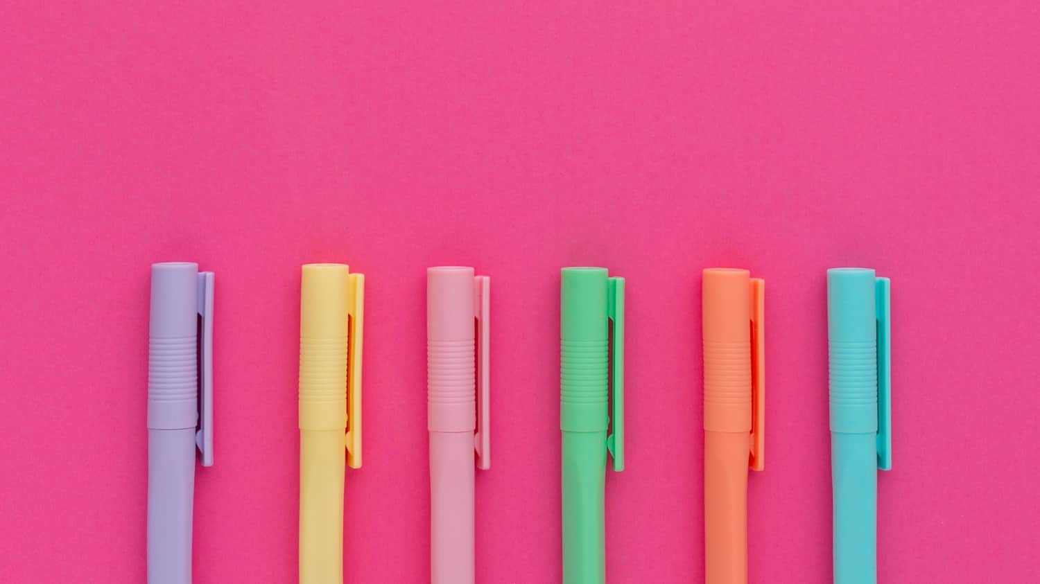 Colorful pens on a bright pink background, showcasing pastel stationery for creative marketing ideas.