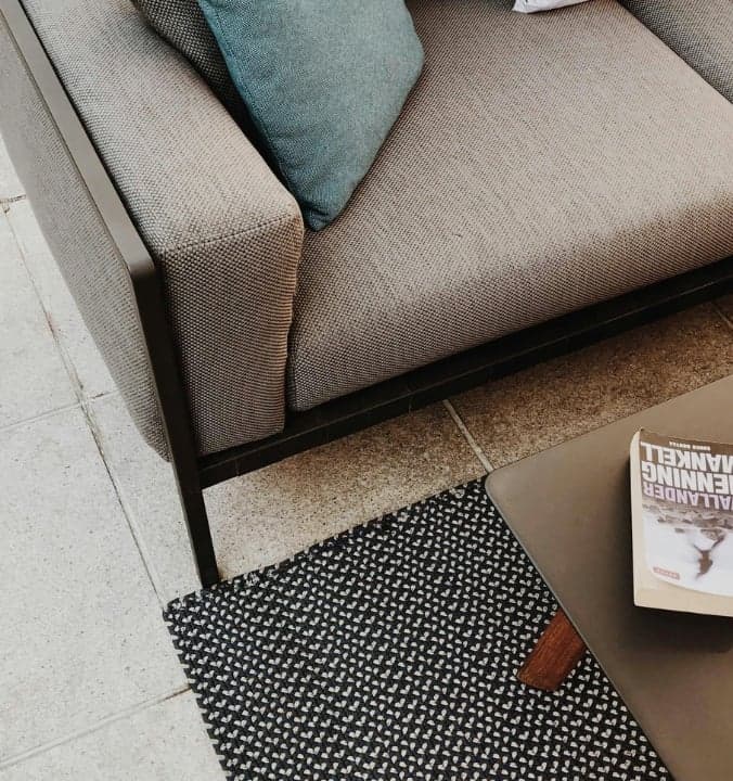 Modern outdoor seating area with a gray sofa, blue cushion, and book titled "Black Hammer" on a table for relaxed...