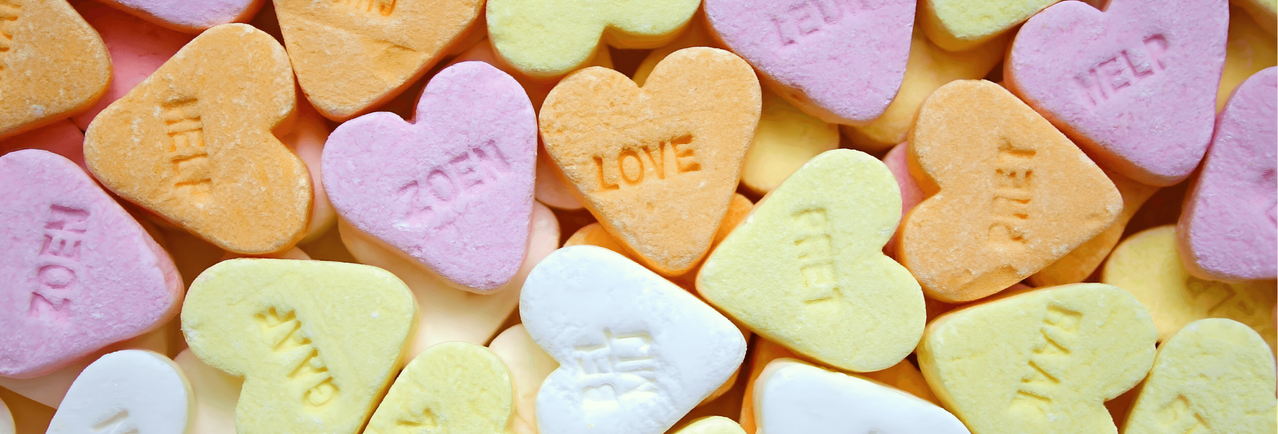 Conversation hearts candy with printed messages in pink, yellow, white and peach colors