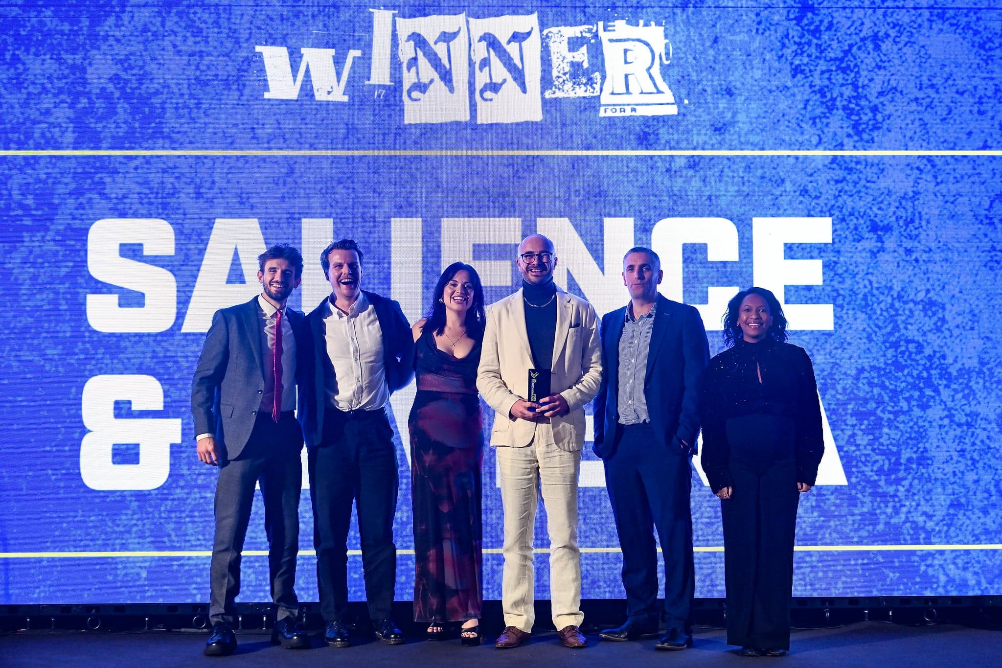 Salience search marketing team celebrates at industry awards event on stage with blue winner backdrop