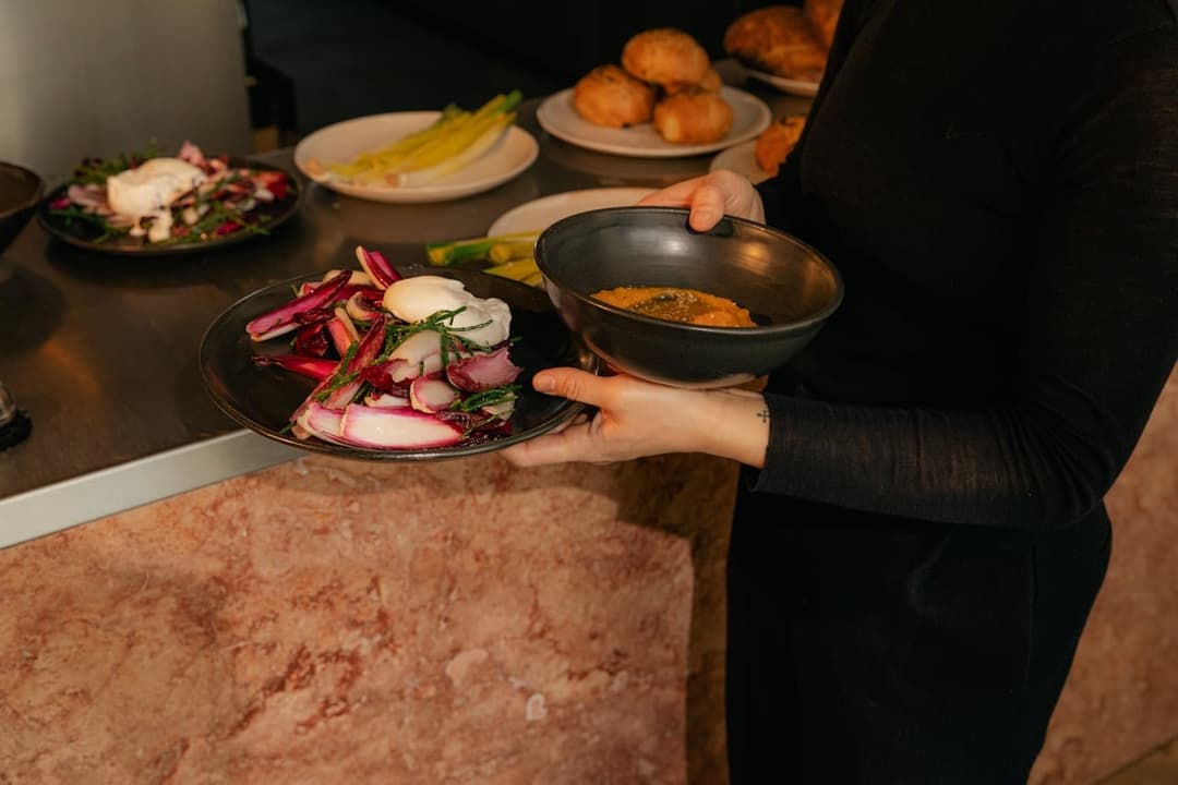 Server holding plate of roasted peppers and onions with prepared curry dish at event