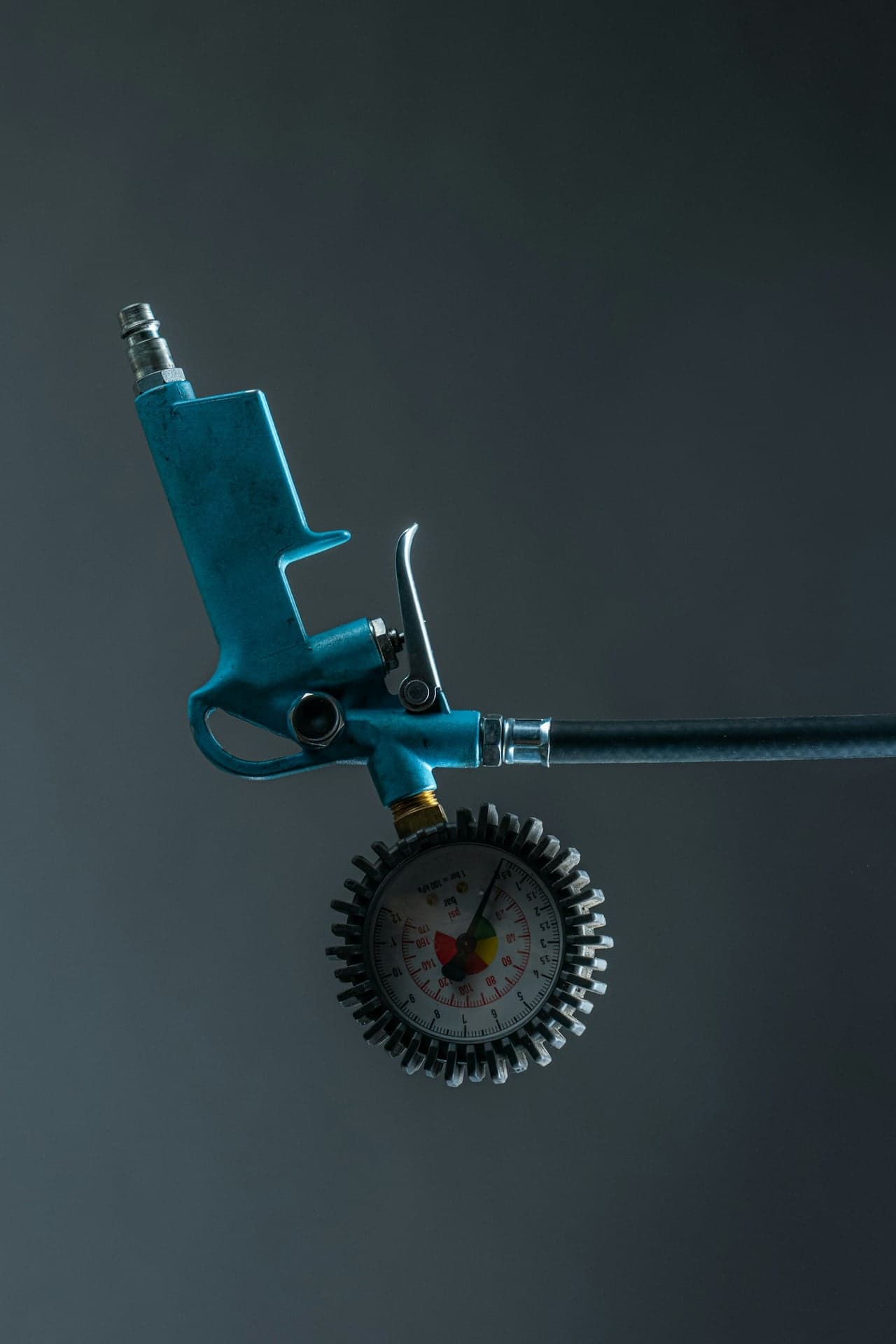 Air pressure gauge with blue handle against dark background adjusting tire pressure.