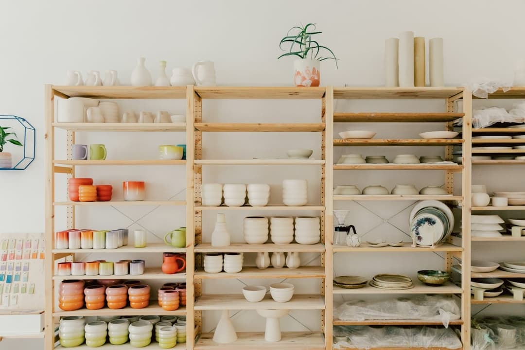 White and colored porcelain bowls and vessels displayed on wooden shelves in a showroom