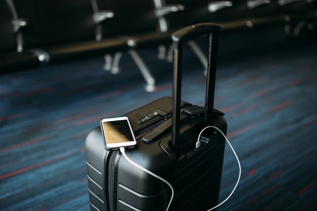 Smartphone showing travel booking information on carry-on luggage with headphones