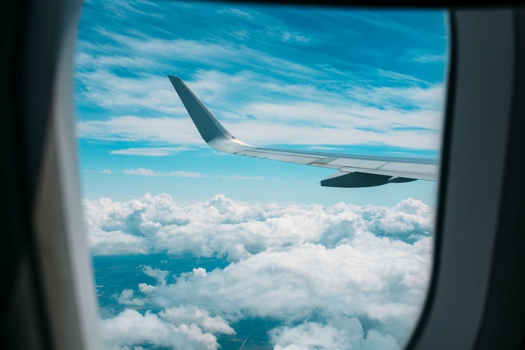 Turquoise ocean and clouds below airplane wing during travel flight