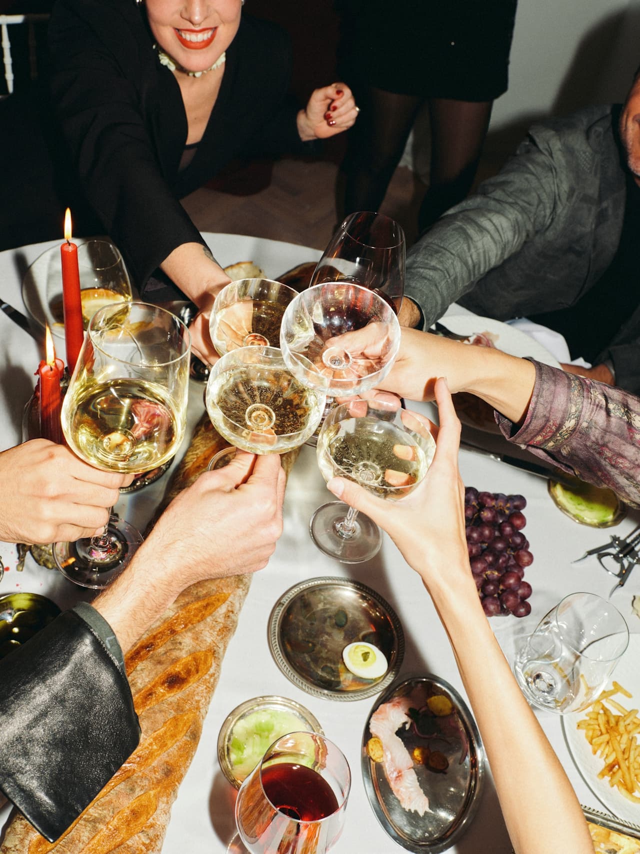 People toasting with wine glasses at a festive dinner table with food and candles.