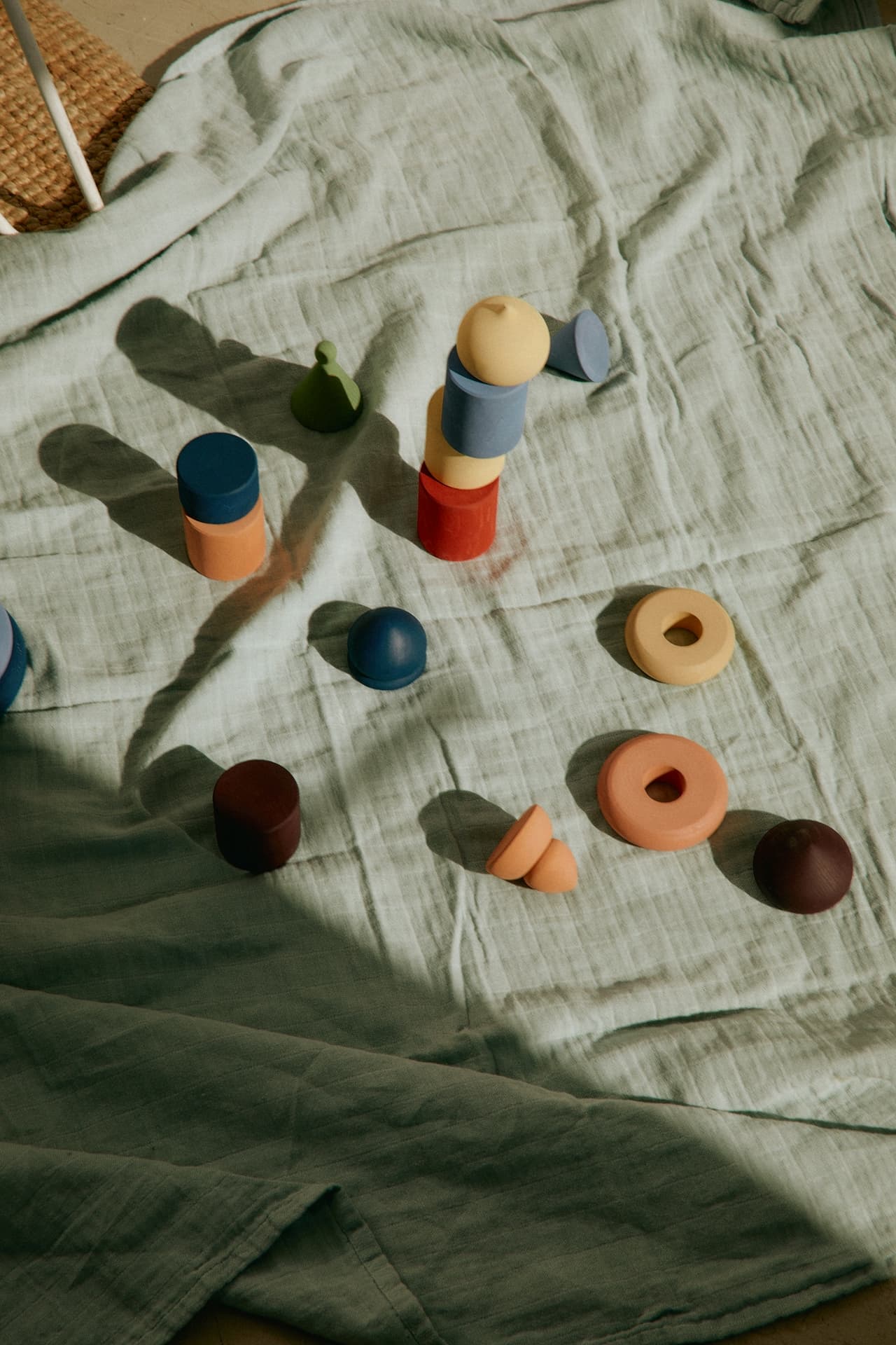 Colorful stacking toys on a crumpled blanket in sunlight.