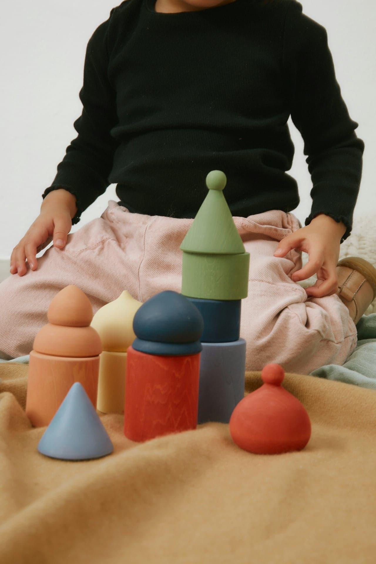 Child playing with colorful geometric wooden blocks on a beige blanket.