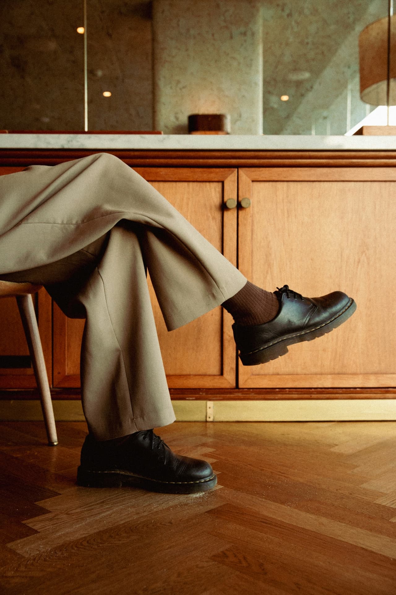Person in brown trousers sitting on chair, wearing black shoes in a stylish office setting.