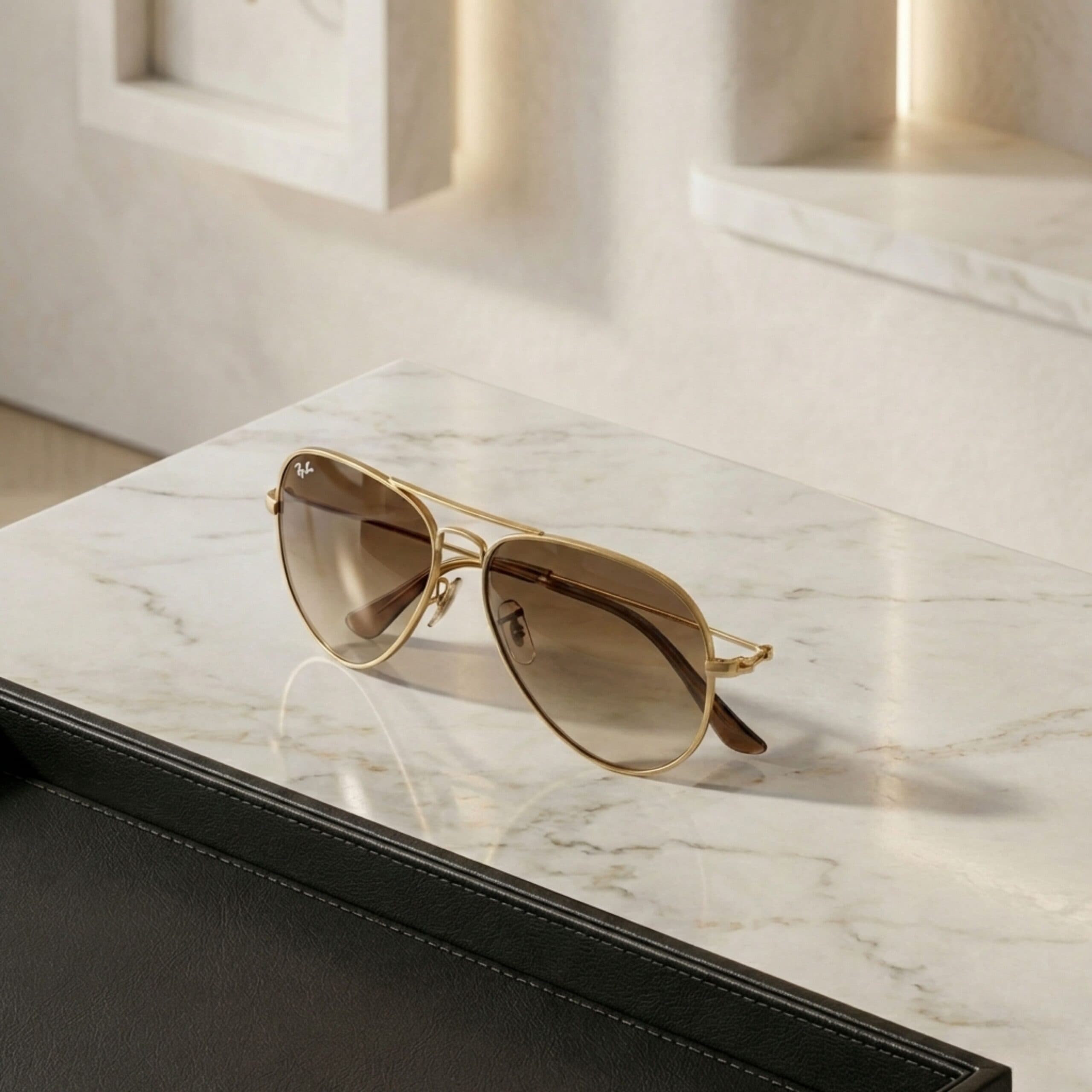 Gold-rimmed aviator sunglasses with brown lenses on a marble surface.