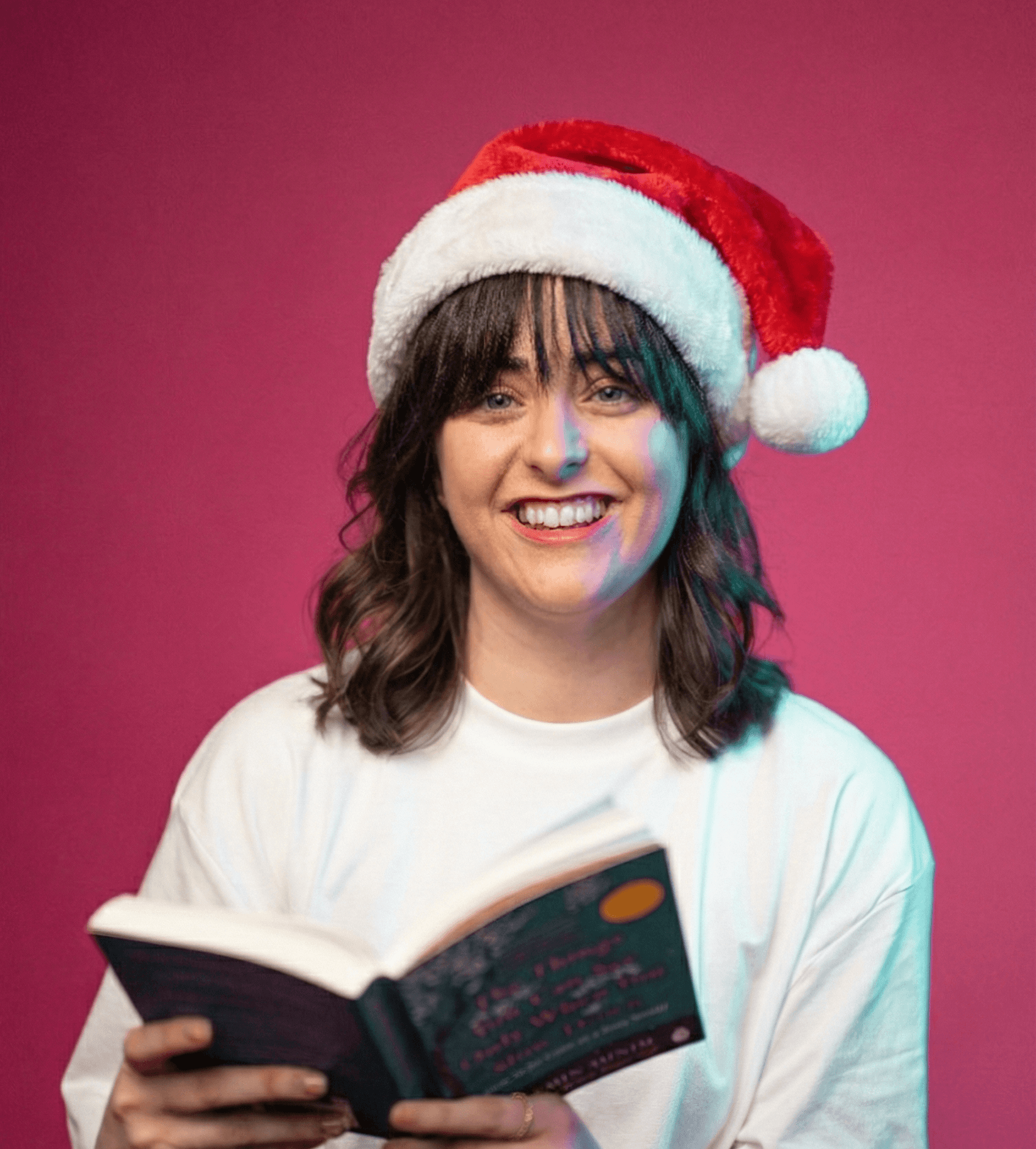 Woman in Santa hat reading book against bright pink background