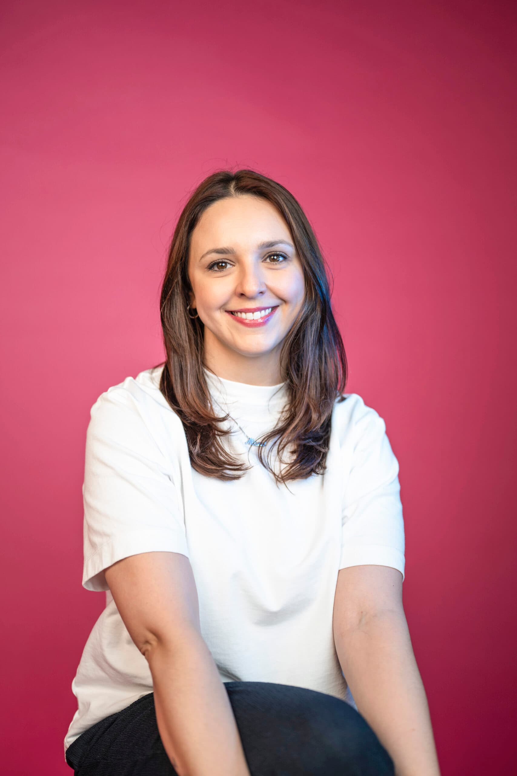 Professional marketing team member with dark hair in studio headshot wearing white shirt against pink background