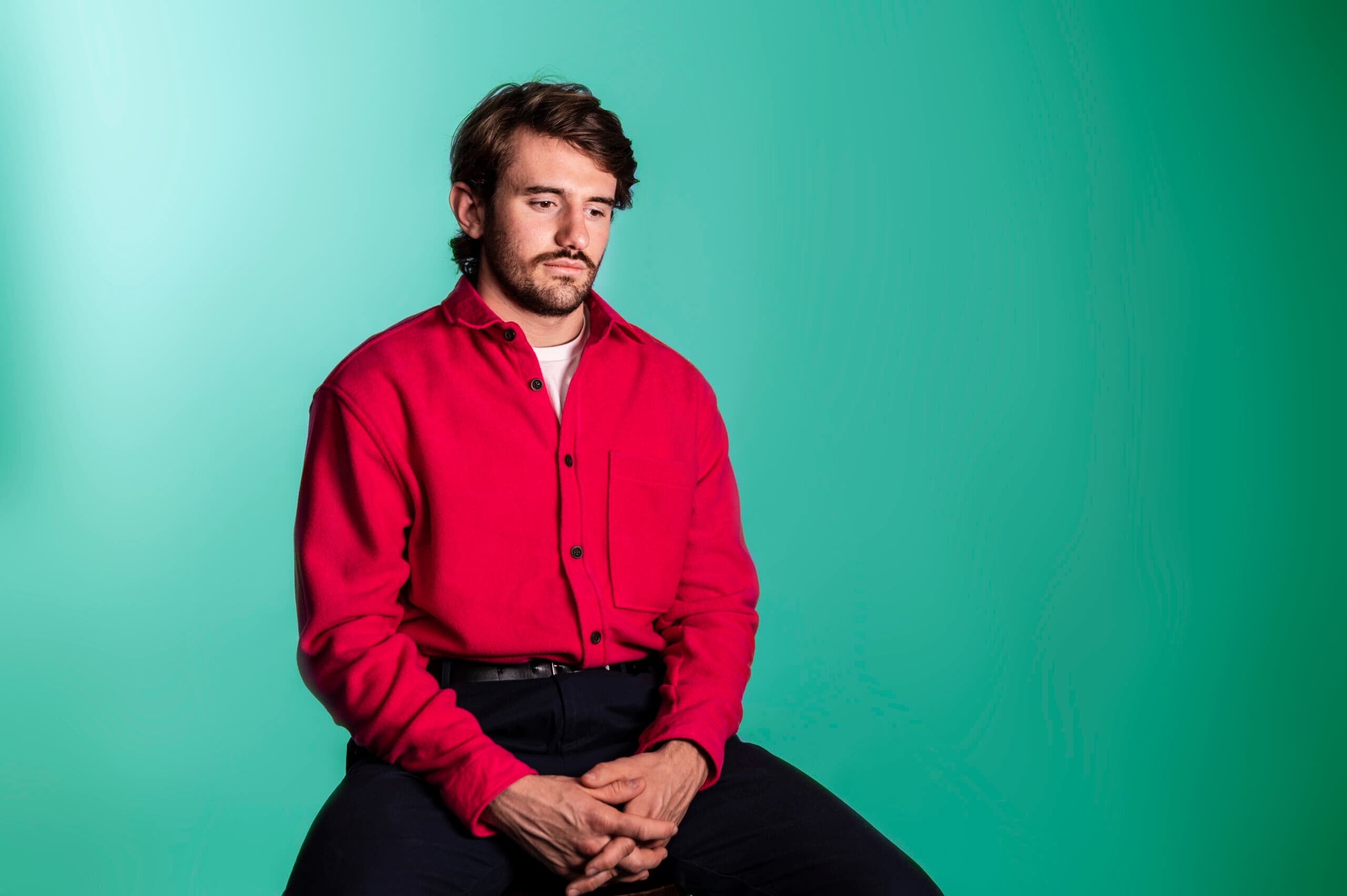 Man in red shirt sitting against turquoise background, representing team member at Salience marketing agency.