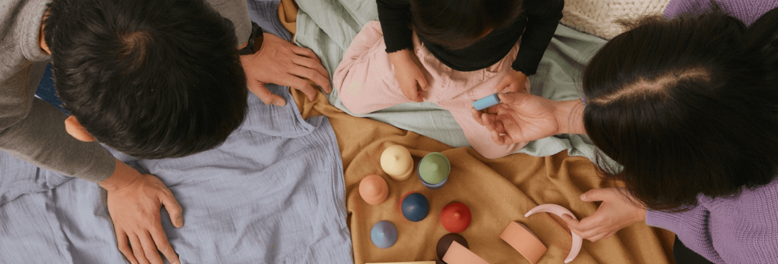 Family playing with colorful wooden toys on blankets, emphasizing creativity in children's activities.
