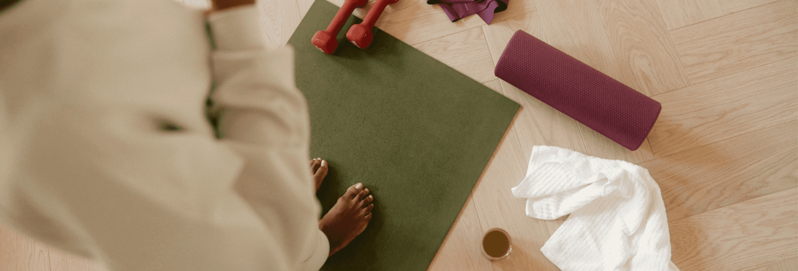 Yoga mat with dumbbells, towel, and cup, highlighting workout setup on wooden floor.