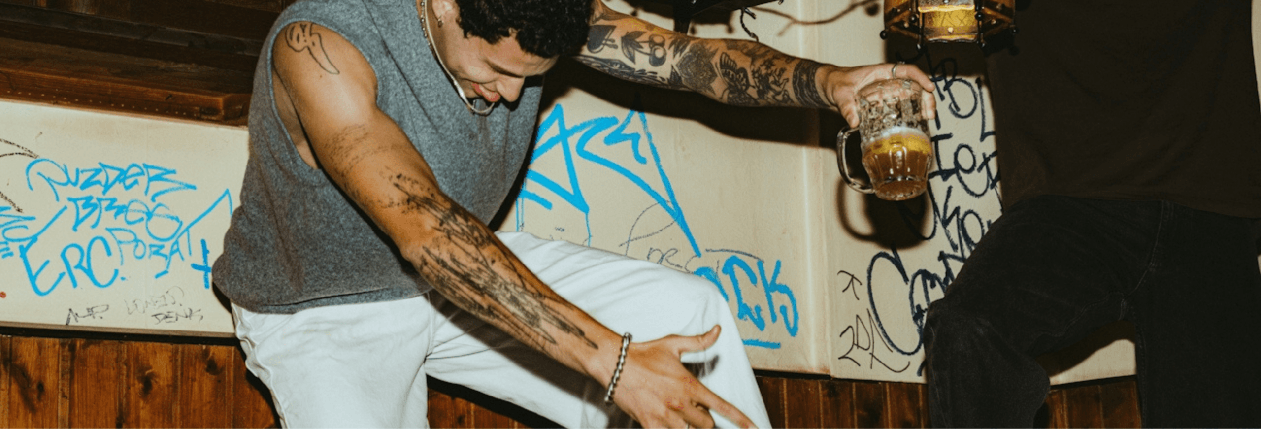 People dancing energetically with drinks in hand, wall graffiti in the background.