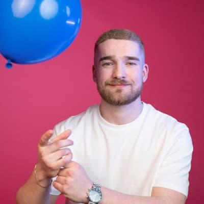 Owen from Salience search marketing agency pointing at camera against pink background with blue balloon