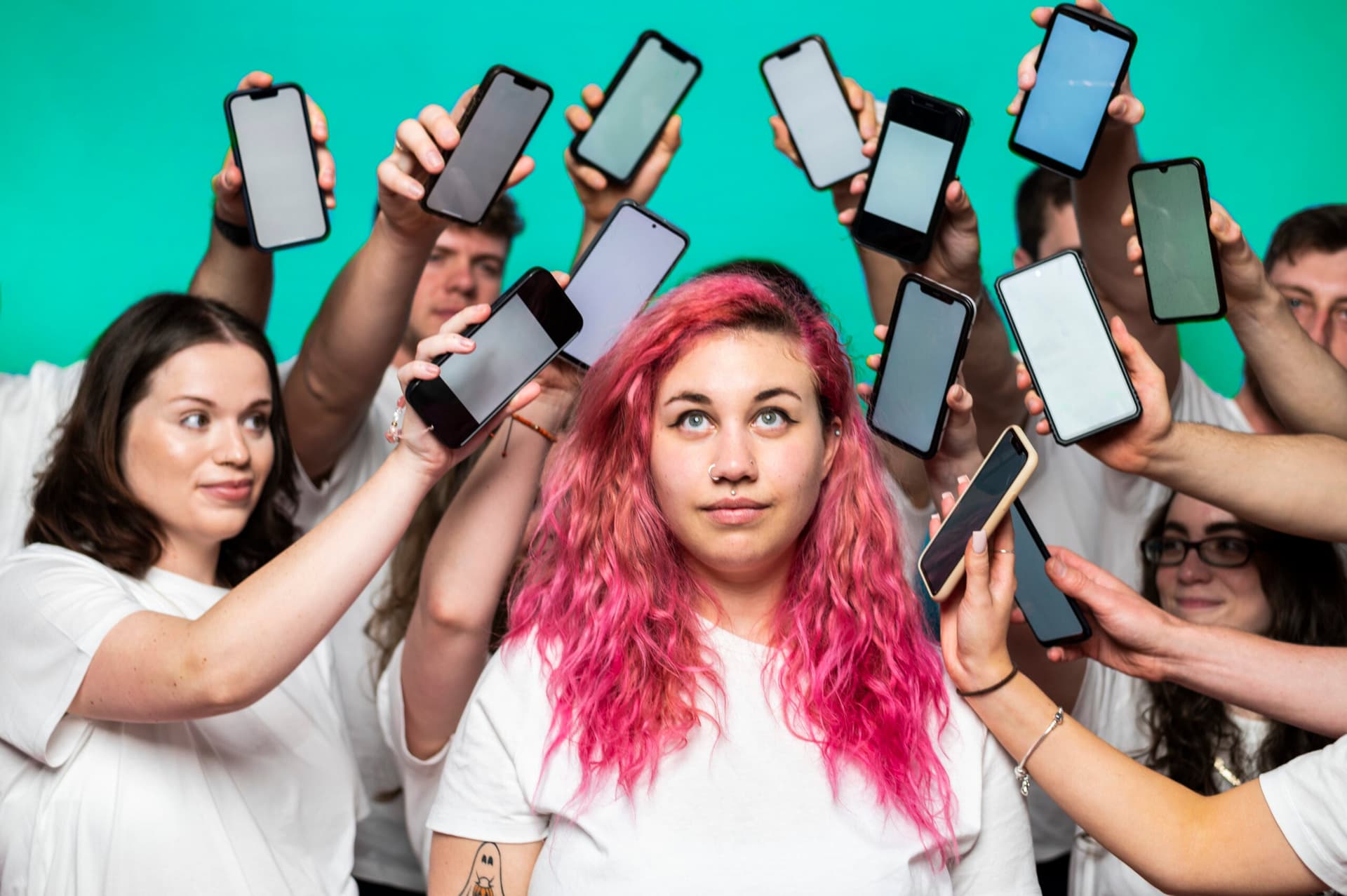 Woman with pink hair surrounded by hands holding smartphones, digital engagement concept
