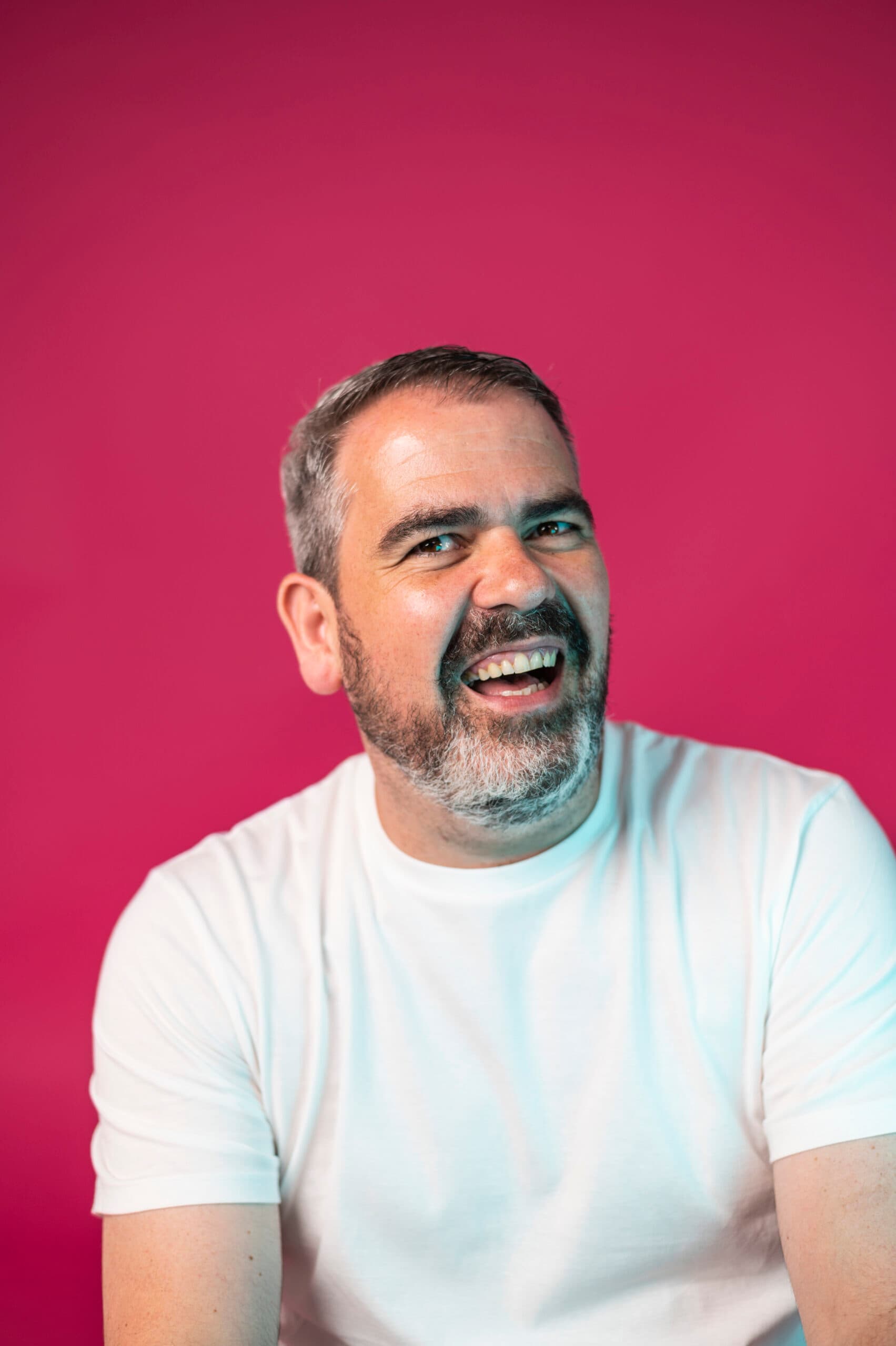 Bearded man in white t-shirt smiling, marketing team headshot