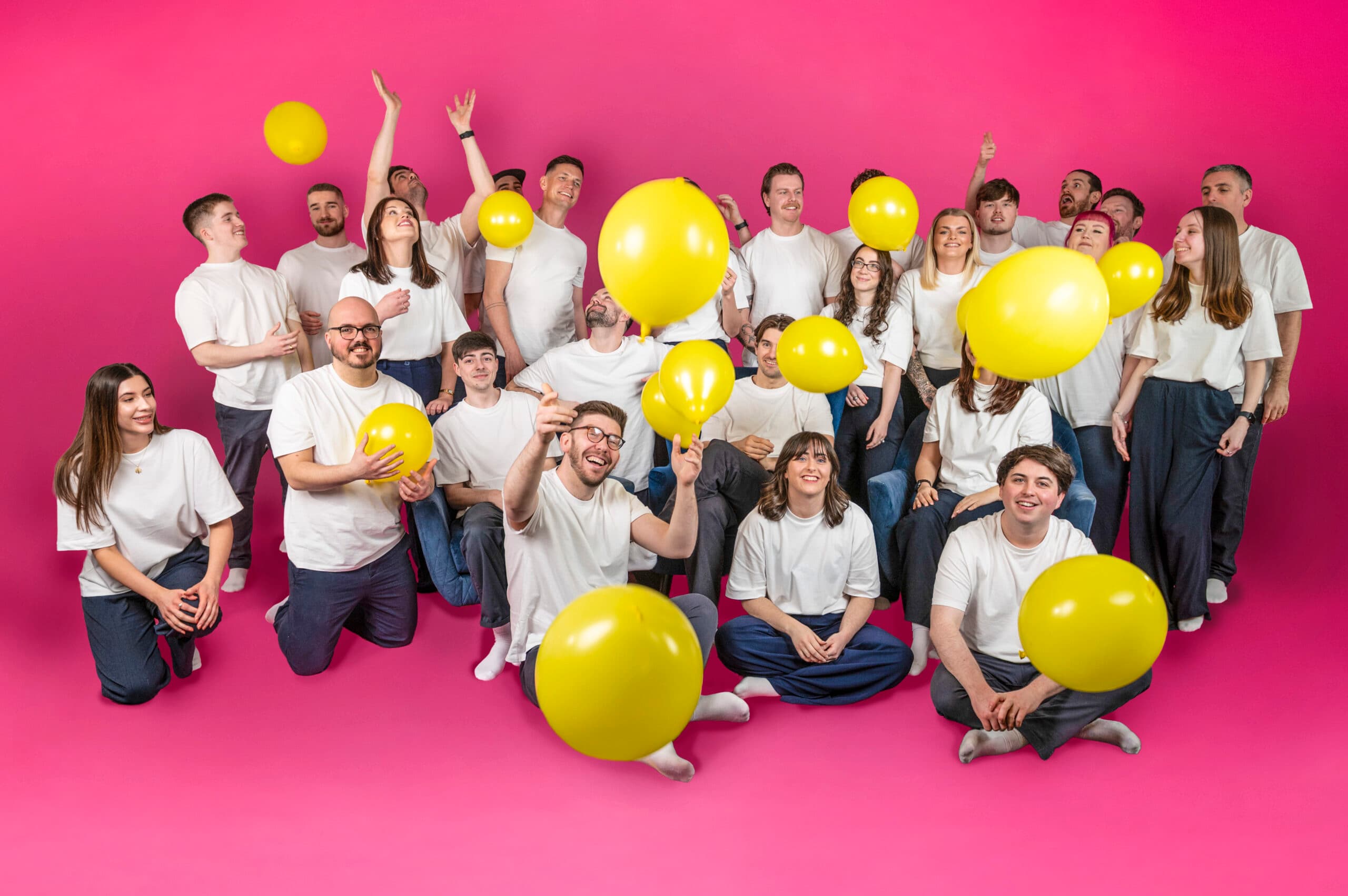 E-commerce agency team celebrating with bright yellow balloons against pink backdrop