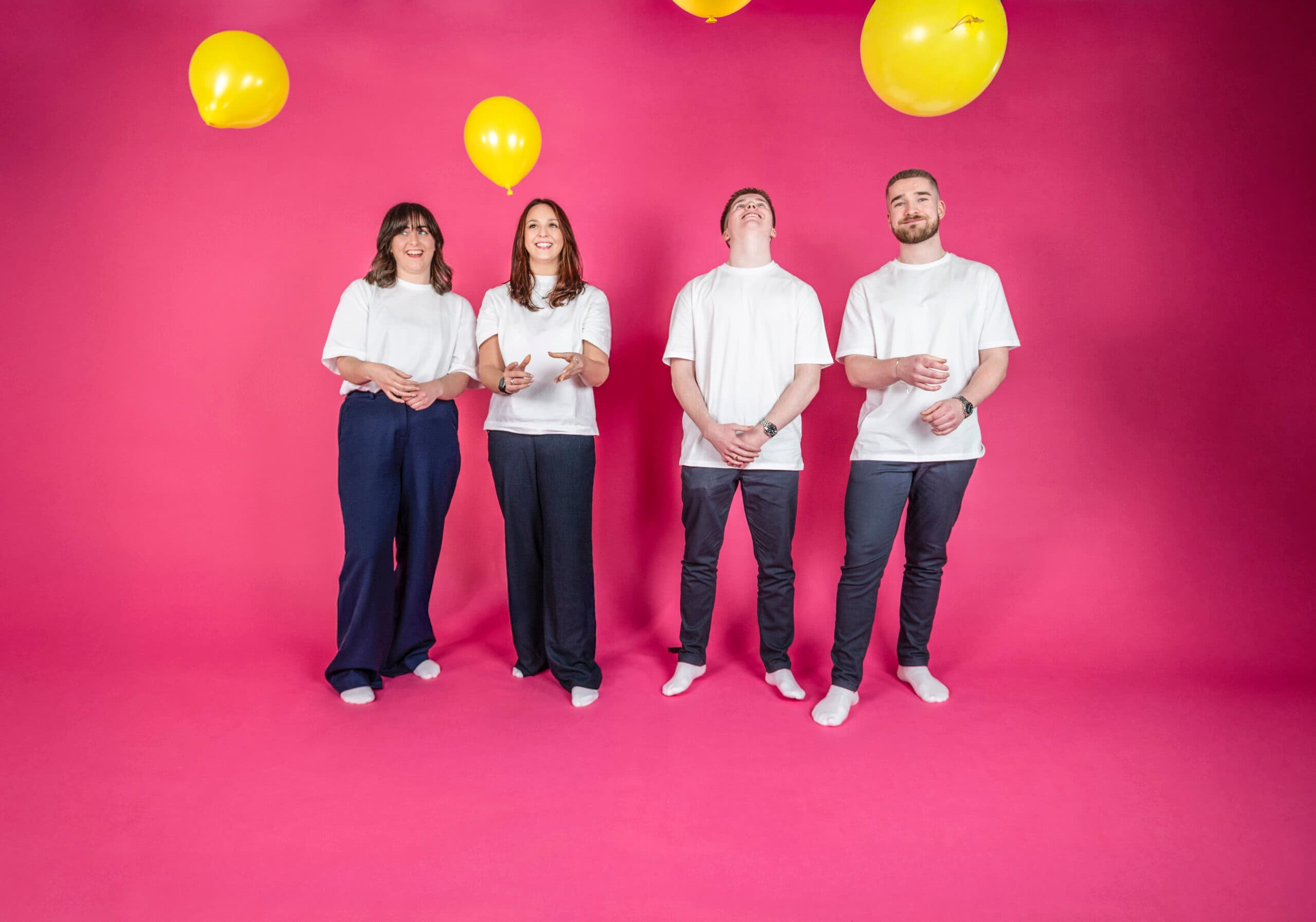 Diverse marketing team of four posing against pink backdrop with yellow balloons