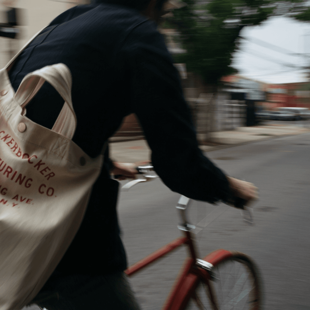 Cyclist riding red bike with branded tote bag in motion on urban street