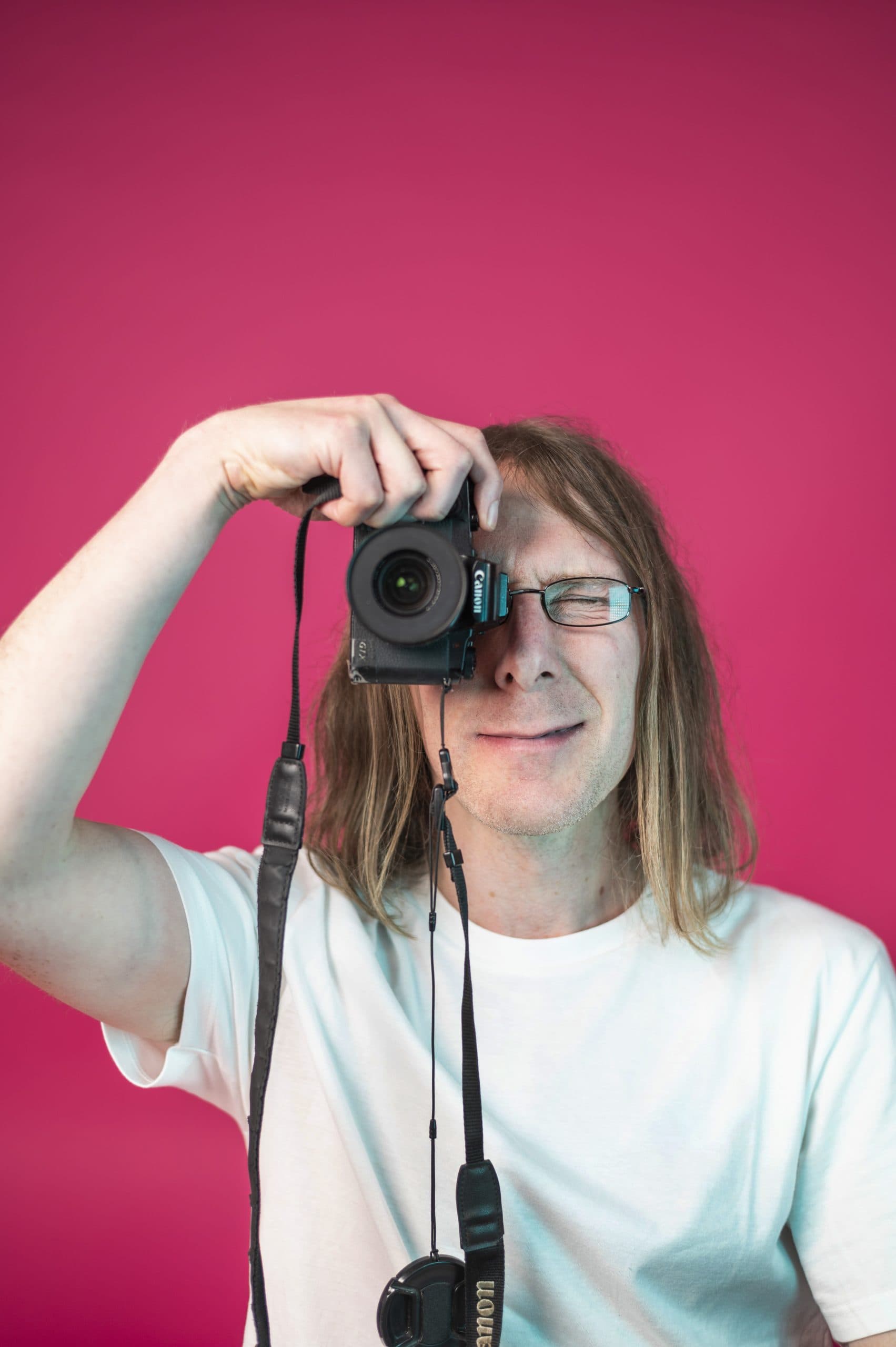 Man with a camera against a pink background in creative marketing setting.
