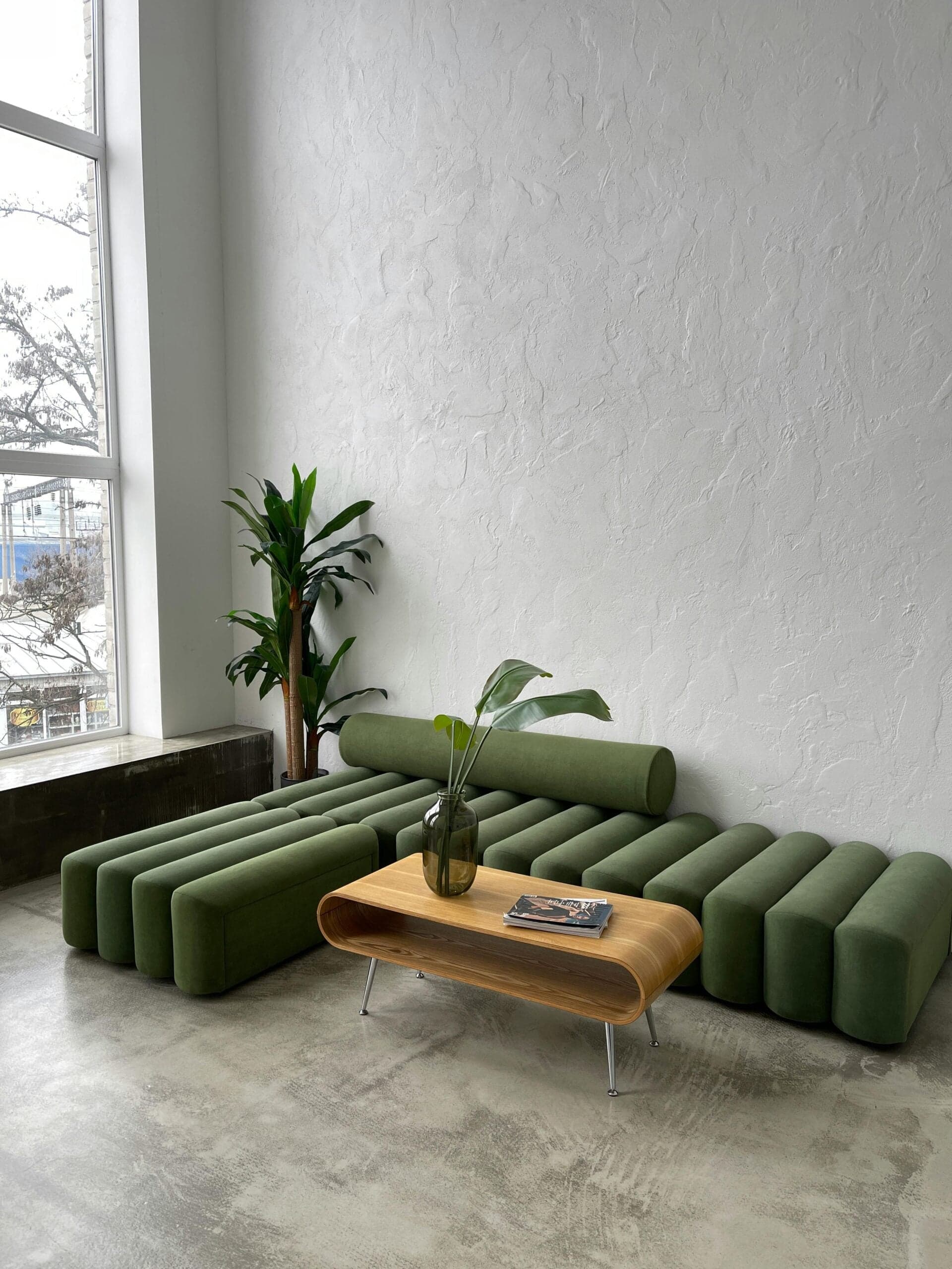 Modern office lounge with emerald green channel-tufted sofa, wooden coffee table, and potted plants