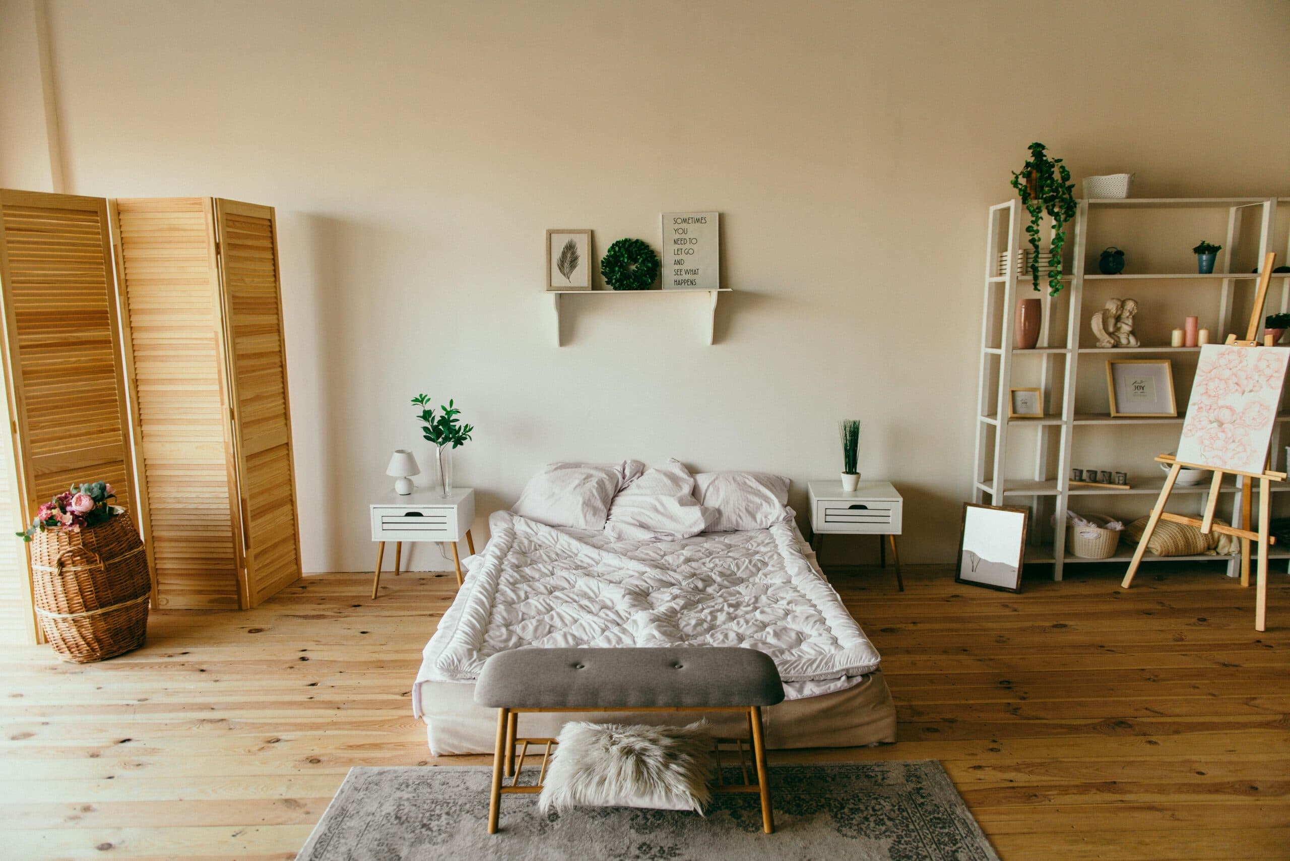 Modern minimalist bedroom interior with wooden floors, white bedding, potted plants, and wall shelving