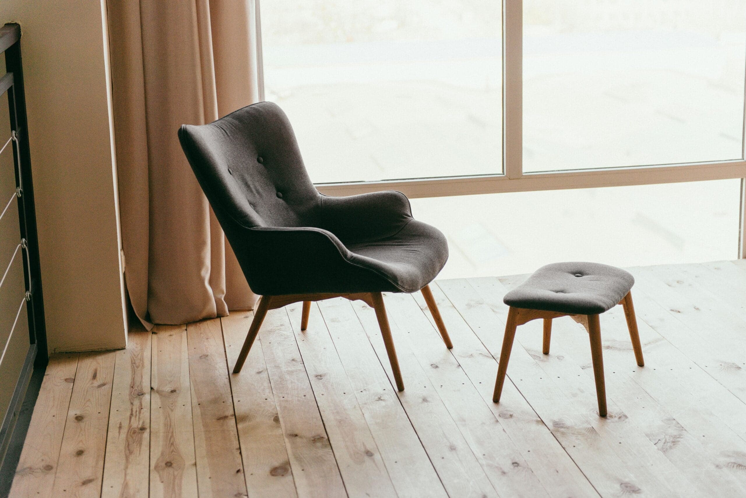 Dark gray mid-century modern chair with matching ottoman on light wooden floor, minimalist interior design