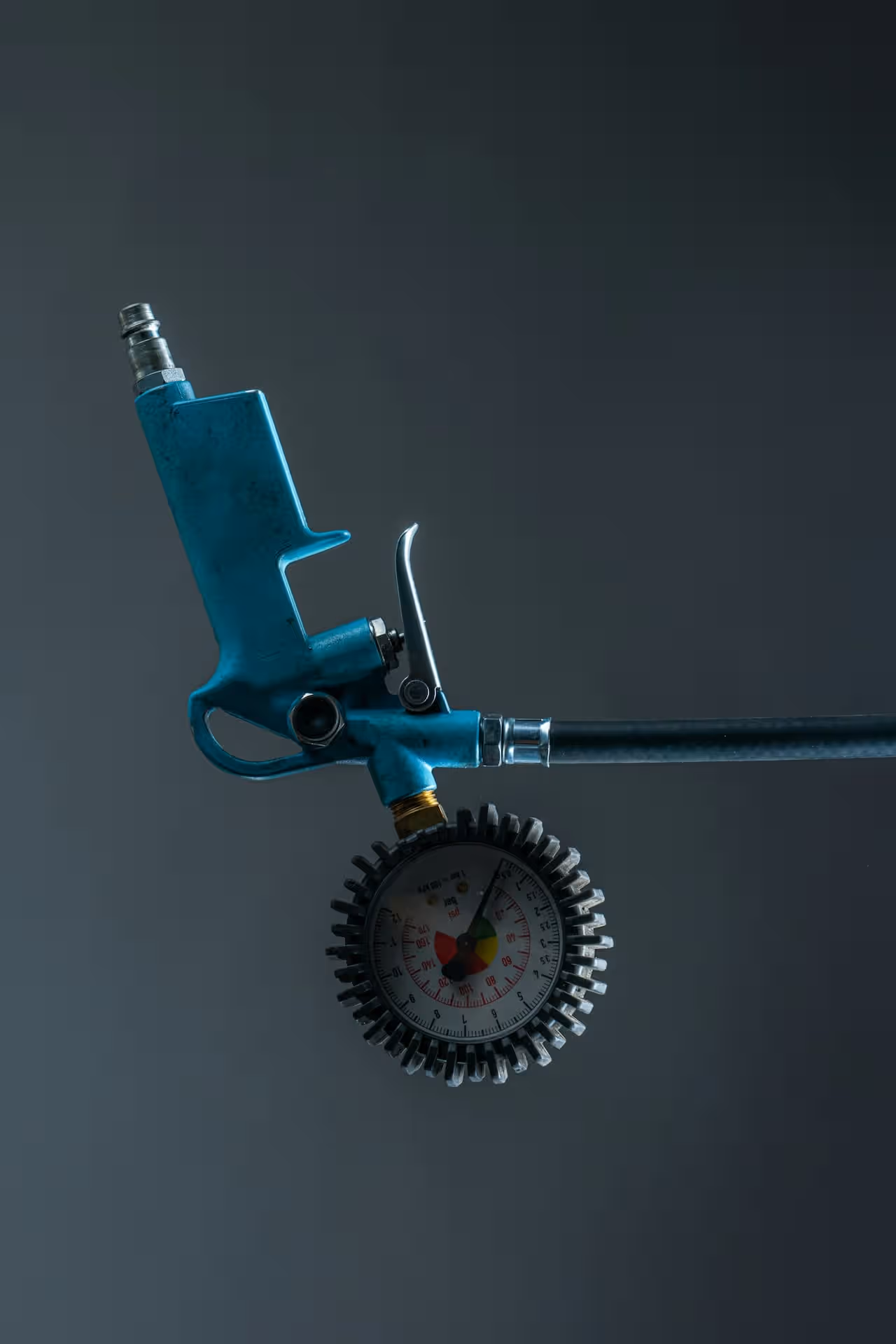 Air pressure gauge with blue handle against dark background adjusting tire pressure.