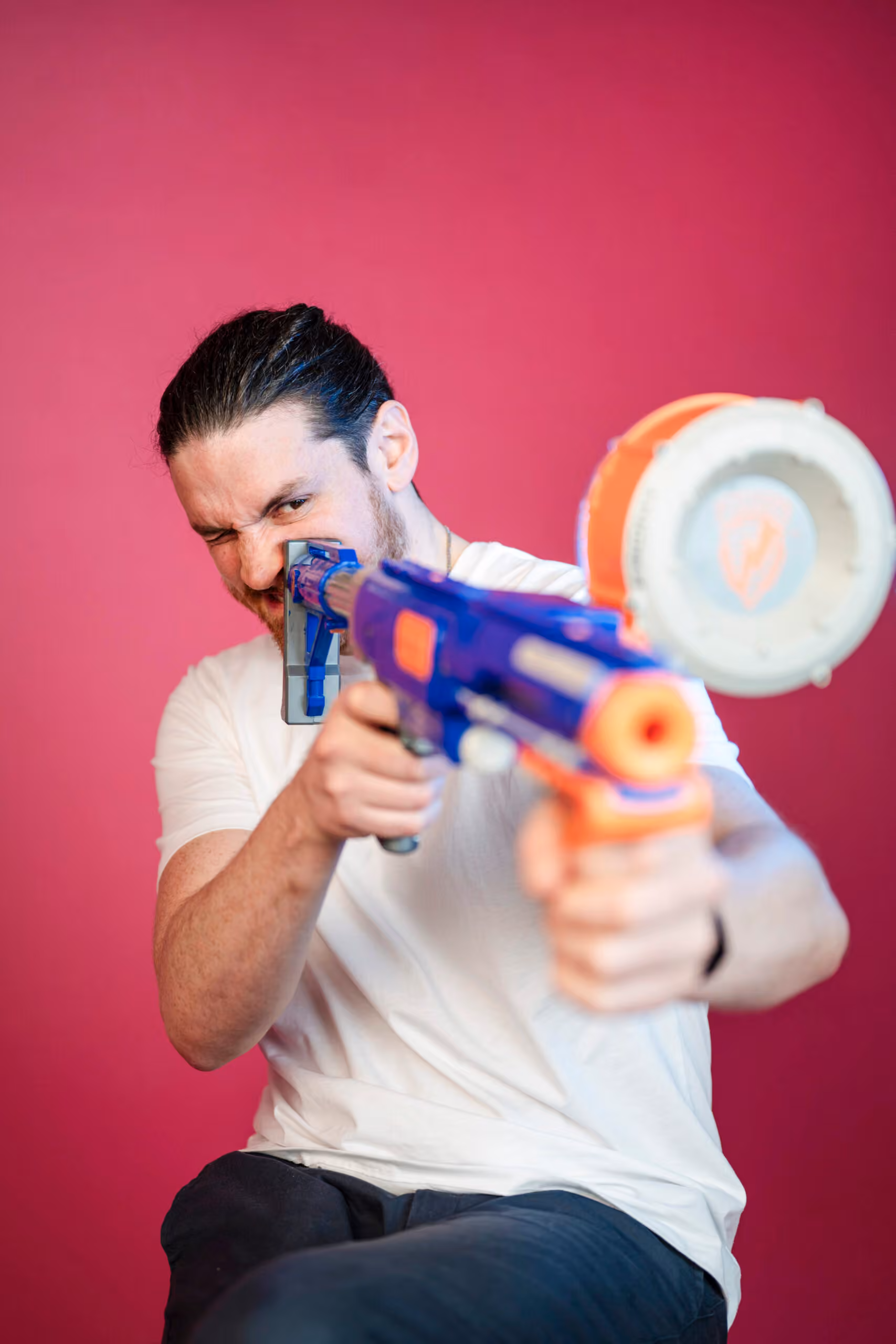 Professional headshot with man aiming blue toy gun on pink background