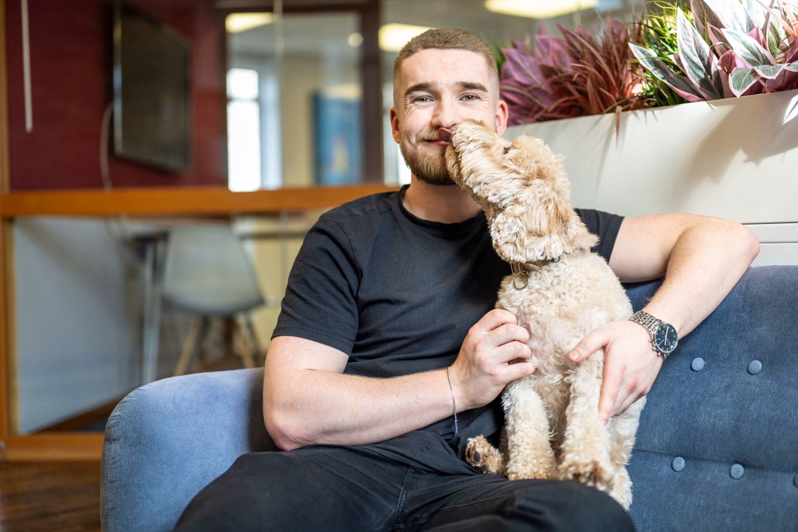 Man on a couch with a curly-haired dog in a friendly office setting at Salience marketing agency.